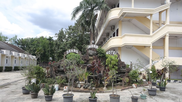 Entrada de un hotel con un letrero que dice "INDAH HOTEL" y varias plantas en macetas al frente.