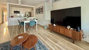 Un salon moderne doté d’un téléviseur à écran plat, d’un meuble de rangement en bois et d’un coin repas avec une table et des chaises.