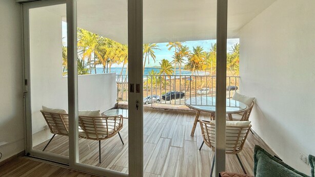 Une pièce dotée d’une porte-fenêtre coulissante donnant sur un balcon avec une piscine, des palmiers et une vue sur l’océan.