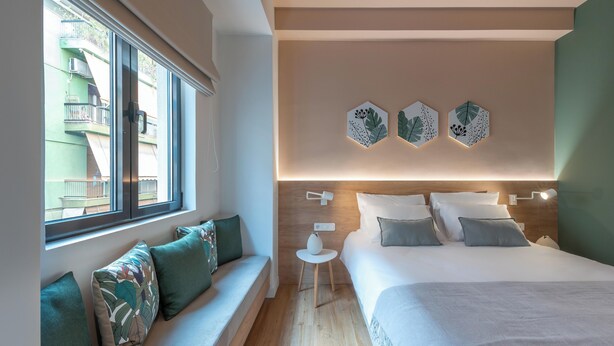 A modern hotel room with a large bed, a seating area with a view of the outside, and decorative wall art. - Corto Maltese (Athens)