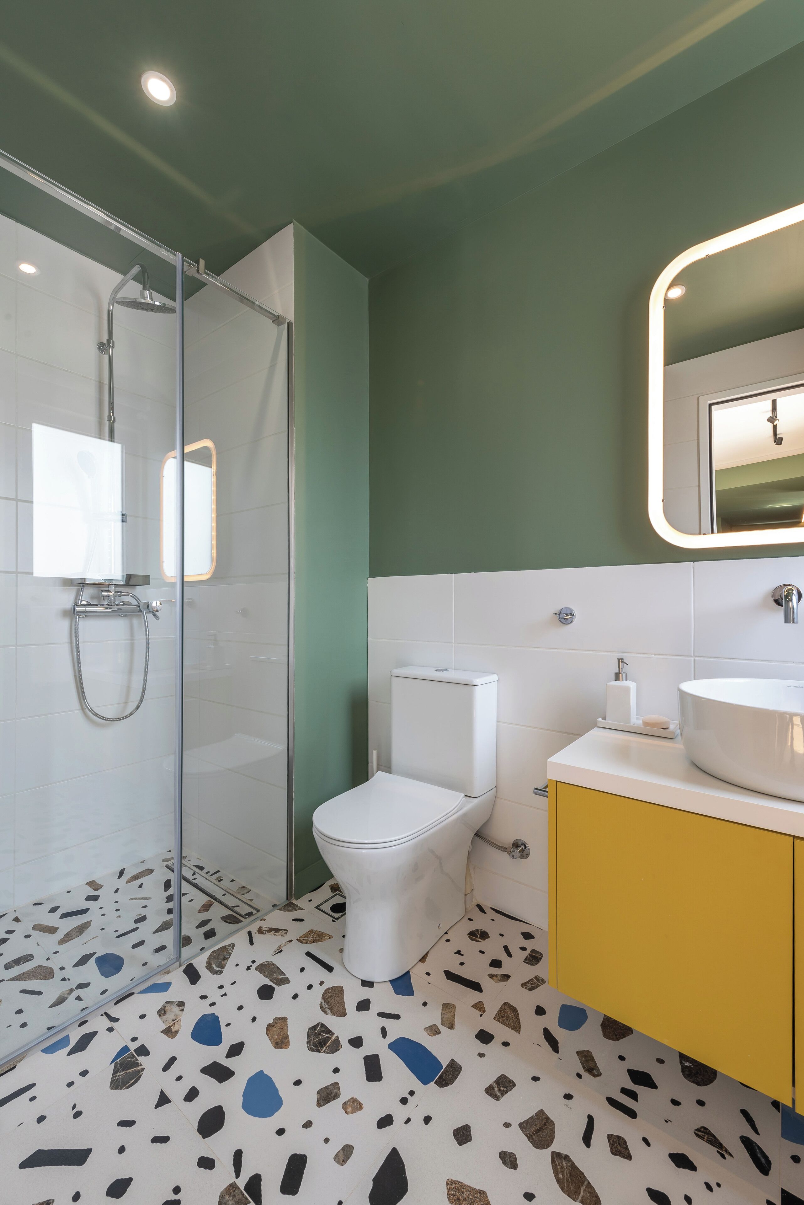A modern bathroom with a glass-enclosed shower, a white toilet, and a yellow vanity with a round sink.