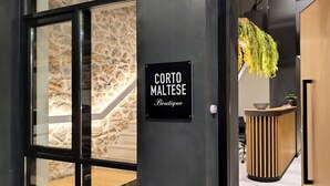 A boutique hotel entrance with a stone wall, a reception desk, and a sign reading "CORTO MALTESE Boutique". - Corto Maltese (Athens)