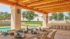 An outdoor dining area with a table set for four, stone walls, and a view of a pool and greenery. - Villa in Ostuni with 3 bedrooms sleeps 6 (Ostuni)