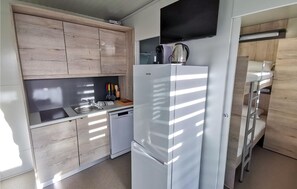 Eine kleine Küche mit Holzschränken, einem weißen Kühlschrank, einer Spüle und einer Kaffeemaschine.