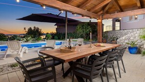 Une terrasse extérieure avec une table et des chaises en bois, une piscine et un mur en pierre.