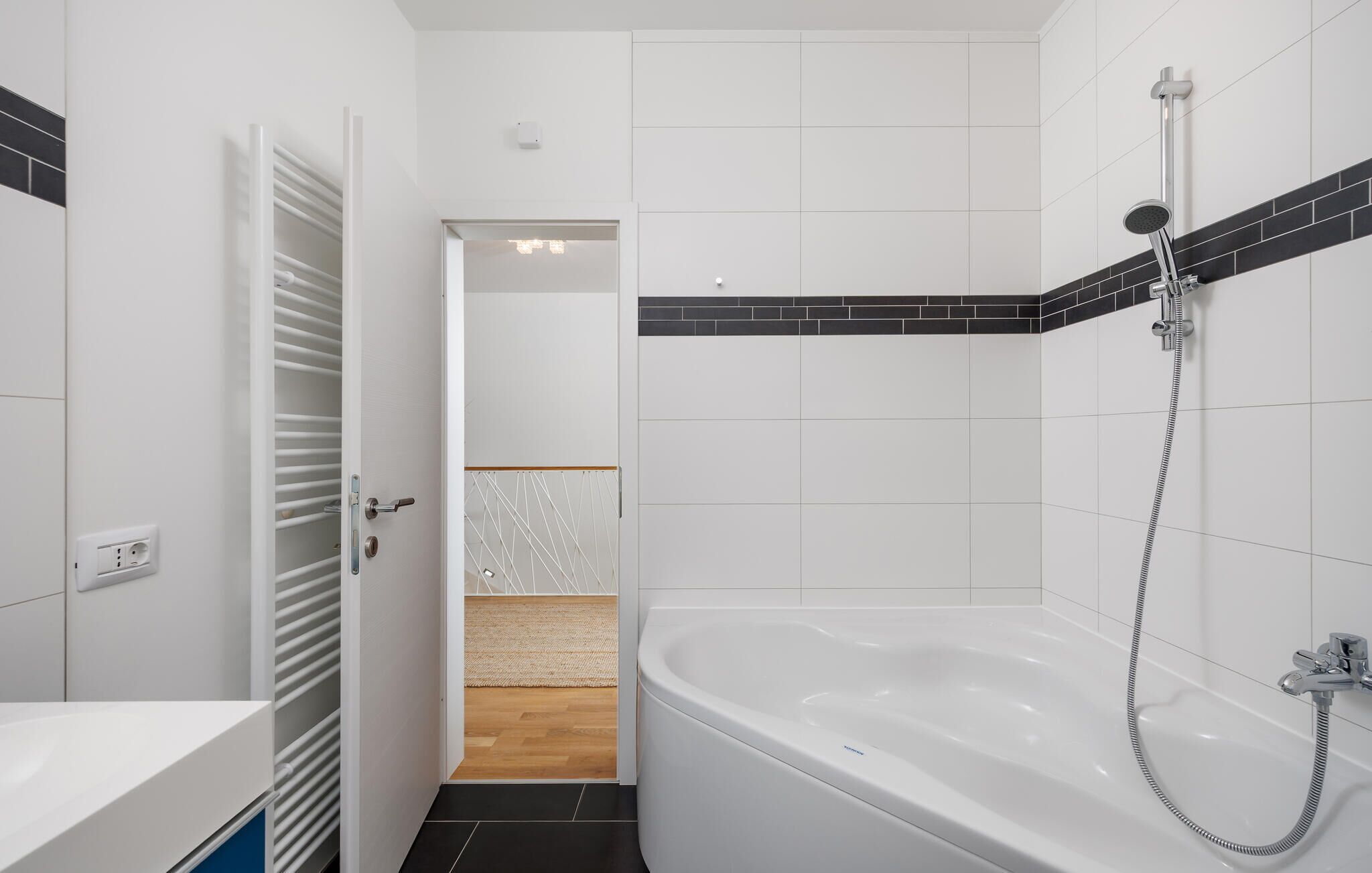 A modern bathroom with a white bathtub, a shower, and a door leading to a hallway.
