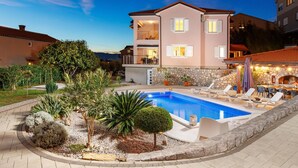 Une maison à deux étages avec une piscine, un espace extérieur aménagé et un mur en pierre.