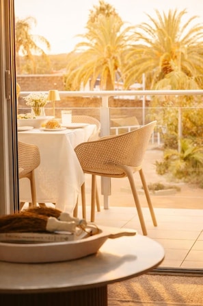 An outdoor dining area with tables and chairs, a view of palm trees, and a balcony railing. - The Oaks Pacific Blue 1 Bedroom Apartment (Salamander Bay)