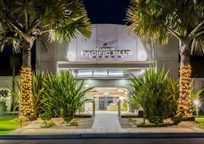 Das Außengelände des DAKS Pacific Blue Resort mit einem Weg zum Eingang, umgeben von Palmen und gepflegter Bepflanzung.