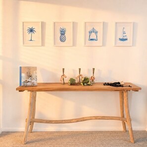 A wooden table with a book and decorative items against a wall with four framed artworks. - The Oaks Pacific Blue 1 Bedroom Apartment (Salamander Bay)