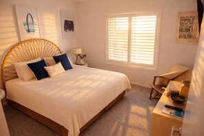 Ein Schlafzimmer mit einem großen Bett, einem Nachttisch, einem Stuhl und einem Fenster mit Jalousien.