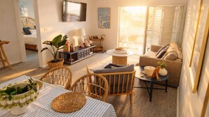 A modern living room with a sofa, chairs, a coffee table, and a TV mounted on the wall. - The Oaks Pacific Blue 1 Bedroom Apartment (Salamander Bay)