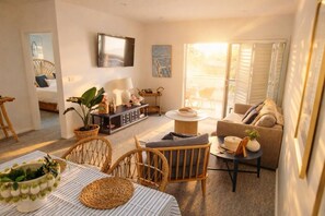 Ein modernes Wohnzimmer mit einer Couch, Sesseln, einem Couchtisch und einem an der Wand befestigten Fernseher.