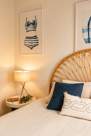 A bedroom with a bed, a bedside table with a lamp, and two framed artworks on the wall. - The Oaks Pacific Blue 1 Bedroom Apartment (Salamander Bay)