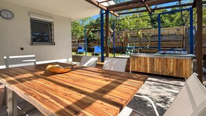 A wooden dining table with chairs, a clock on the wall, and a barbecue area with a wooden fence. - Beautiful home in Drazice (Drazice)