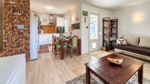 A modern kitchen with white cabinets, a dining area with a wooden table and chairs, a living room with a sofa and a coffee table, and a decorative wall with a heart-shaped arrangement of logs. - Beautiful home in Drazice (Drazice)