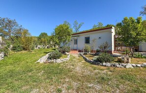 A single-story house with a stone pathway leading to the entrance, surrounded by greenery and trees.
