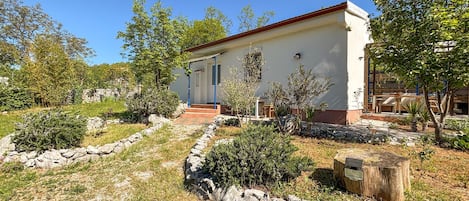 A single-story building with a red roof, surrounded by a garden with various plants and a stone wall.
