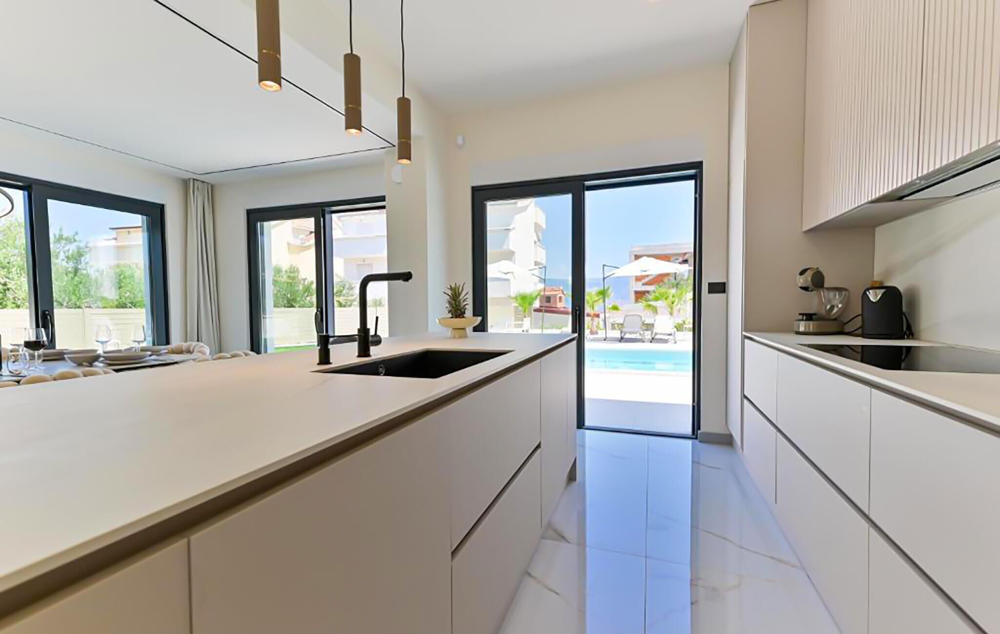 A modern kitchen with a large island, a sink, and a view of a pool and buildings outside.