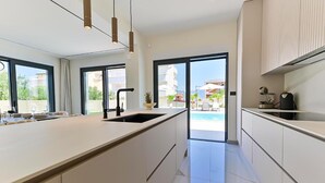 A modern kitchen with a large island, a sink, and a view of a pool and buildings outside. - Stunning home in Slatine (Slatine)