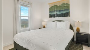 A neatly made bed with a white bedspread, two bedside lamps, and a wall-mounted tapestry. - Covered Pavilion + BBQ | Paso Hillside + Vineyards View | Bombay Chardonnay (Paso Robles)