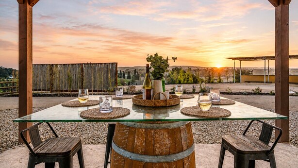 Een terras met een glazen tafel, rieten onderzetters en rustieke stoelen.