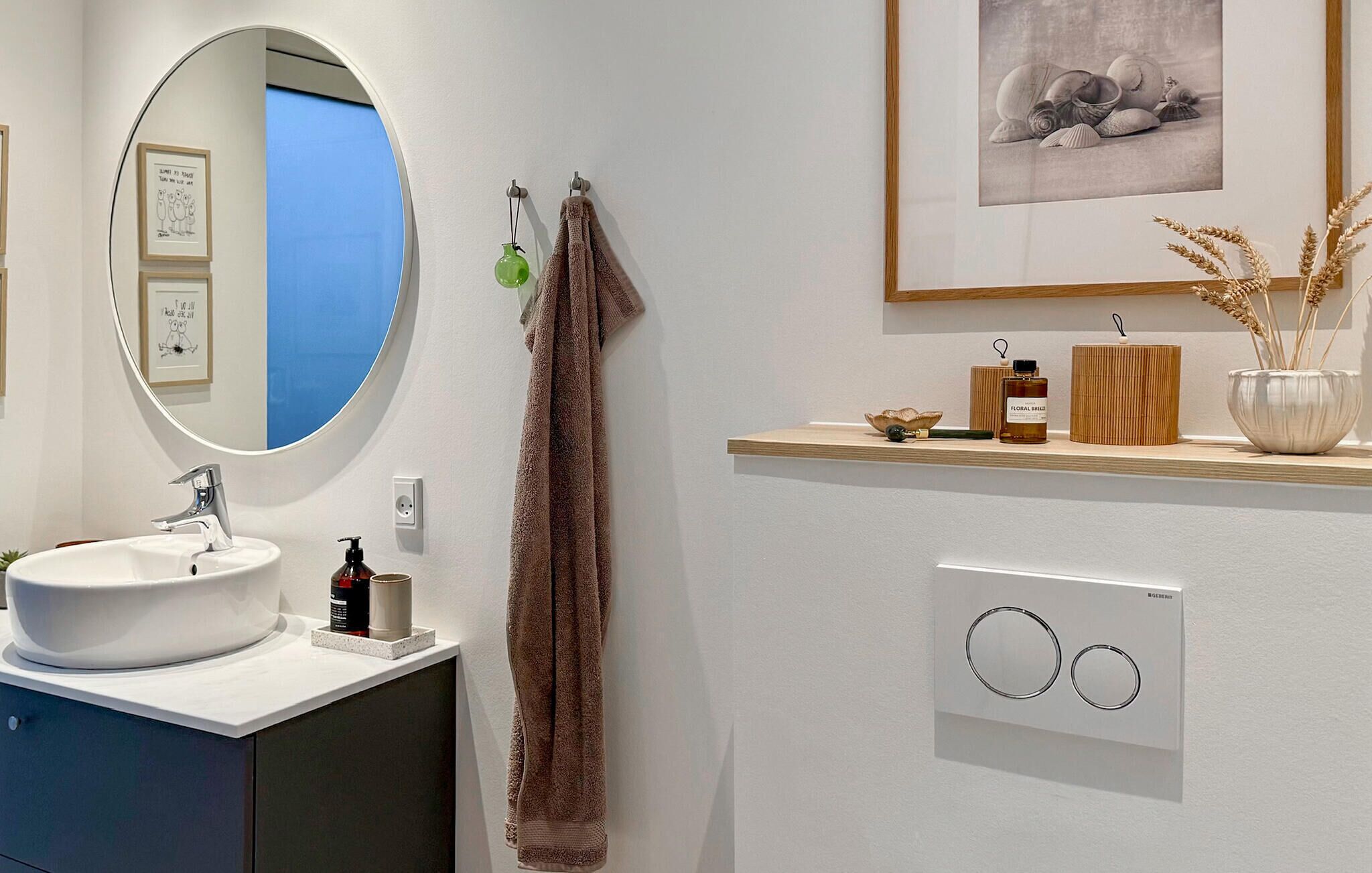 A modern bathroom with a round mirror, white sink, and wooden vanity.