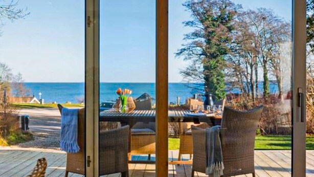 A deck with wicker chairs and a table, overlooking a body of water and trees.