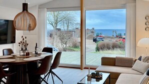 A modern living room with a dining area, large sliding glass doors leading to a view of the sea and construction site.