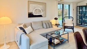 A living room with a sofa, coffee table, and a chair. There is a painting on the wall and a glass cabinet with dishes.