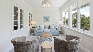 Een kamer met een lichtblauwe bank, rieten stoelen, een ronde tafel en een plafondlamp.