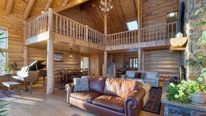 Een ruim houten blokhut interieur met een leren bank, piano en een balkon.