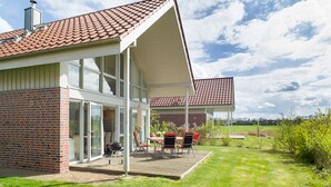 A modern house with a large glass door, a patio with outdoor furniture, and a red-tiled roof. - Gorgeous home in Röbel with sauna (Röbel)