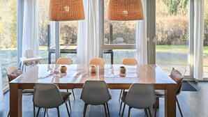 A dining area with a large table, four chairs, two hanging wicker lamps, and large windows offering a view of the outdoors. - Gorgeous home in Röbel with sauna (Röbel)
