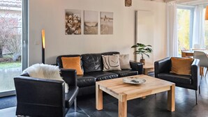 A modern living room with a black leather sofa, a wooden coffee table, and a large window with a view of the outdoors. - Gorgeous home in Röbel with sauna (Röbel)
