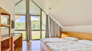 A bedroom with a wooden desk, two beds, a large window with curtains, and a view of greenery. - Gorgeous home in Röbel with sauna (Röbel)