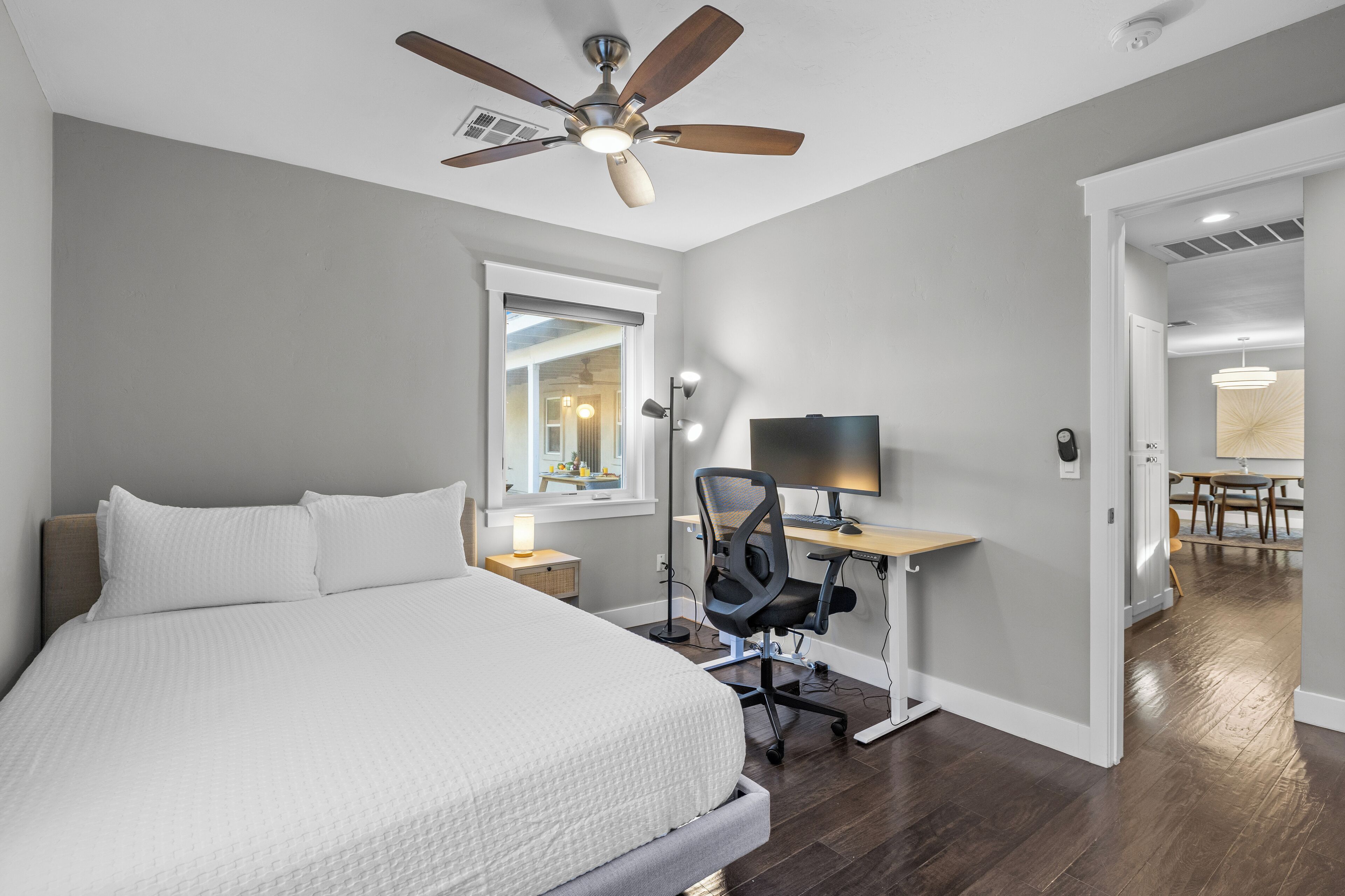 A bedroom with a bed, a desk, a chair, a ceiling fan, and a window.