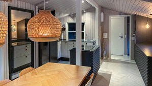 Ett modernt kök med ett matbord i trä, hängande lampor och utsikt över vardagsrummet.