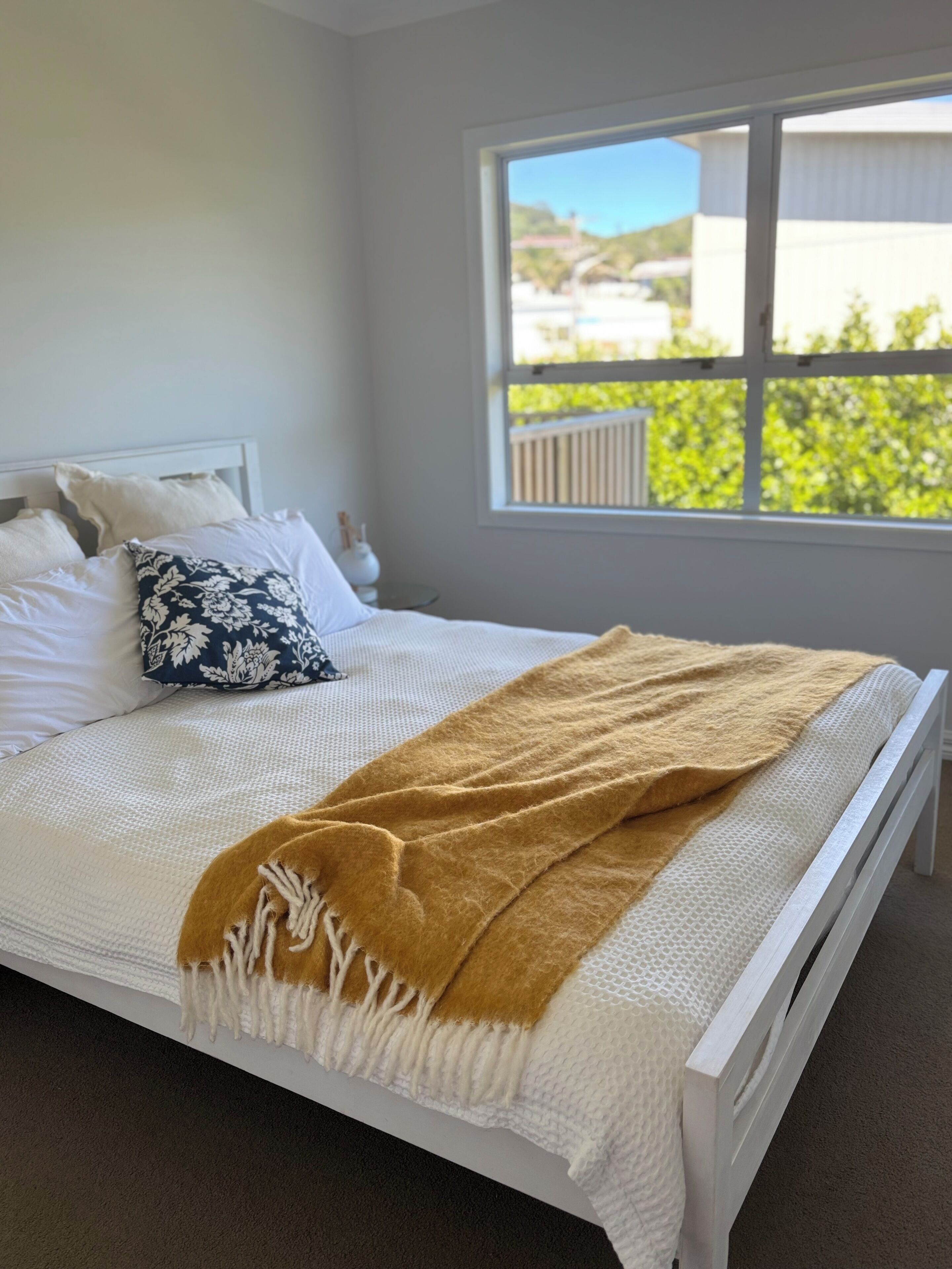 A neatly made bed with a white headboard, a patterned pillow, and a brown throw blanket.