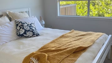 A neatly made bed with a white headboard, a patterned pillow, and a brown throw blanket.