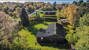A large, single-story house with a sloped roof, surrounded by a well-maintained lawn and dense trees.