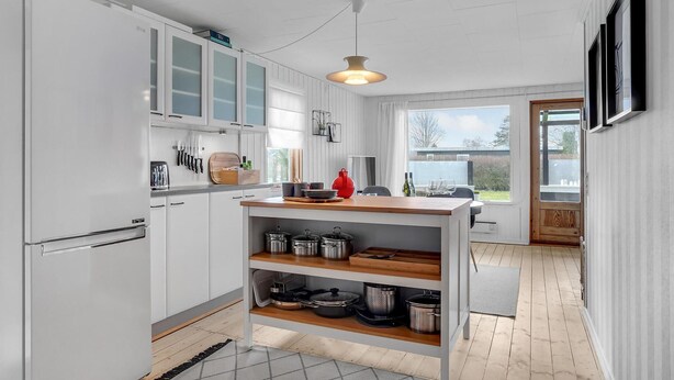A modern kitchen with white cabinets, a central island with a sink, and a view to the outside.