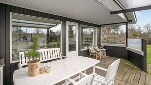 A covered outdoor area with a white table and chairs, a bench, and a potted plant.