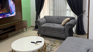 A modern living room with a flat-screen TV, grey sofa, and a white coffee table. - Vine Apartment (Abuja)