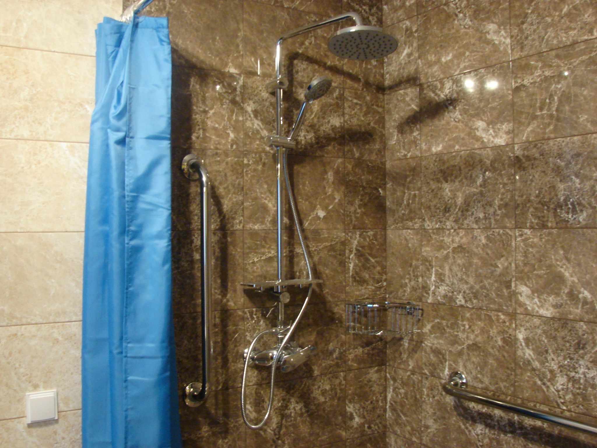A bathroom with a shower, a handrail, and a blue shower curtain.