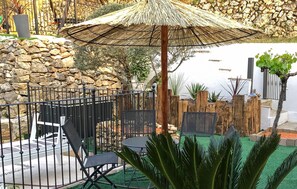 A patio area with a stone wall, a metal fence, a wooden fence, and a thatched umbrella. - Nice home in Gemenos with private swimming pool, can be inside or outside (Gemenos)