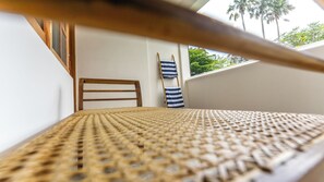 A wicker chair with a striped towel, a wooden chair, and a view of palm trees through a window.