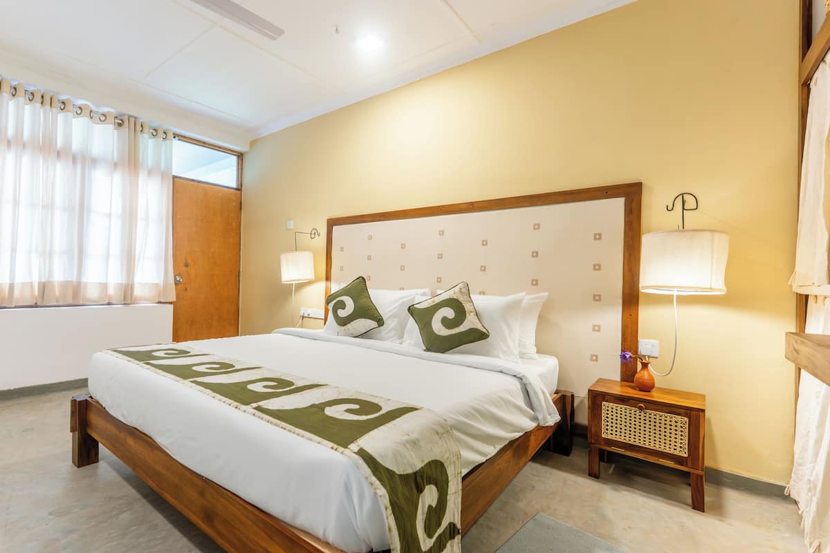 A hotel room with a large bed, two bedside lamps, a wooden headboard, and a window with curtains.