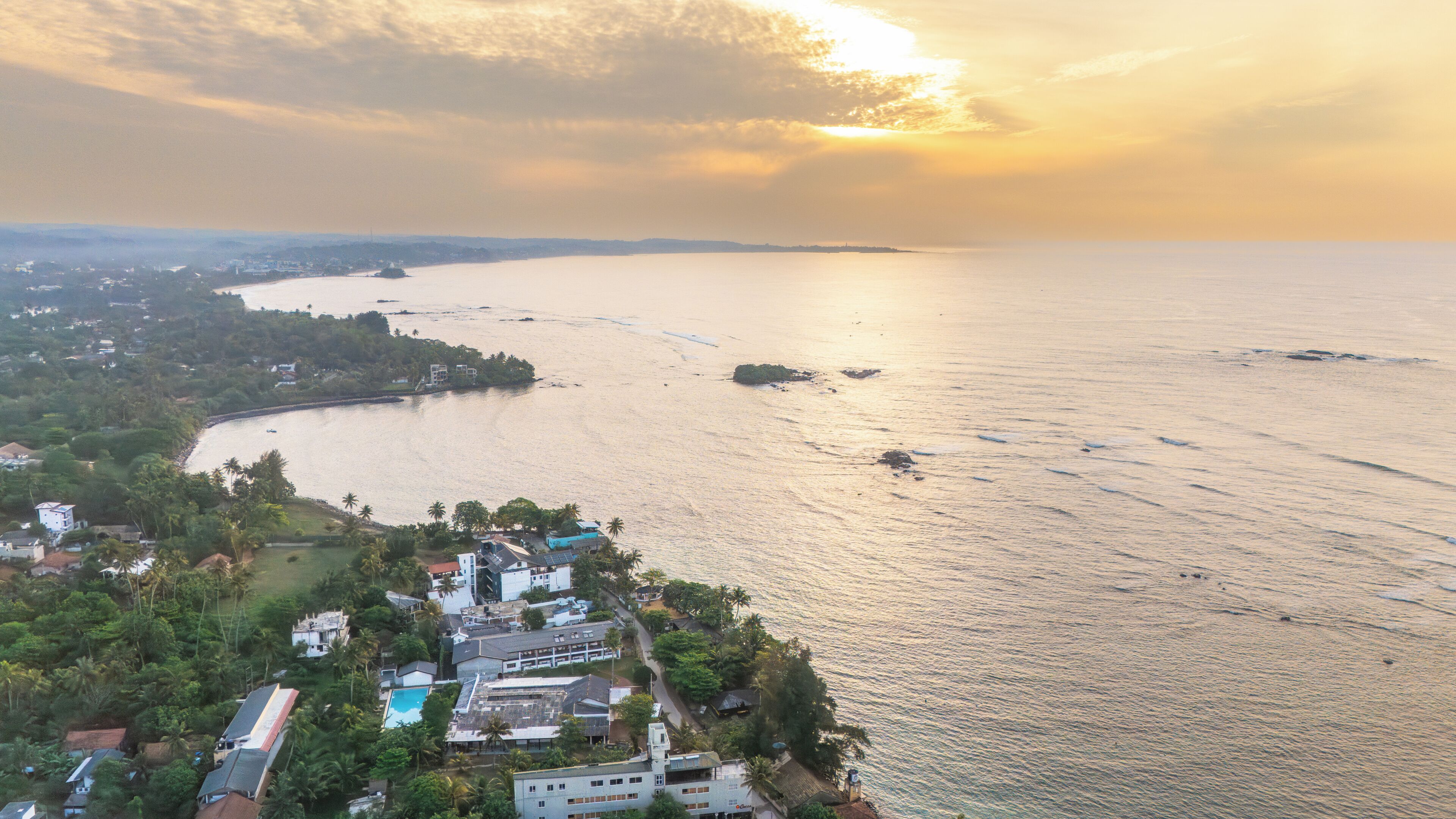 An aerial view of a coastal area with buildings, a beach, and a large body of water.