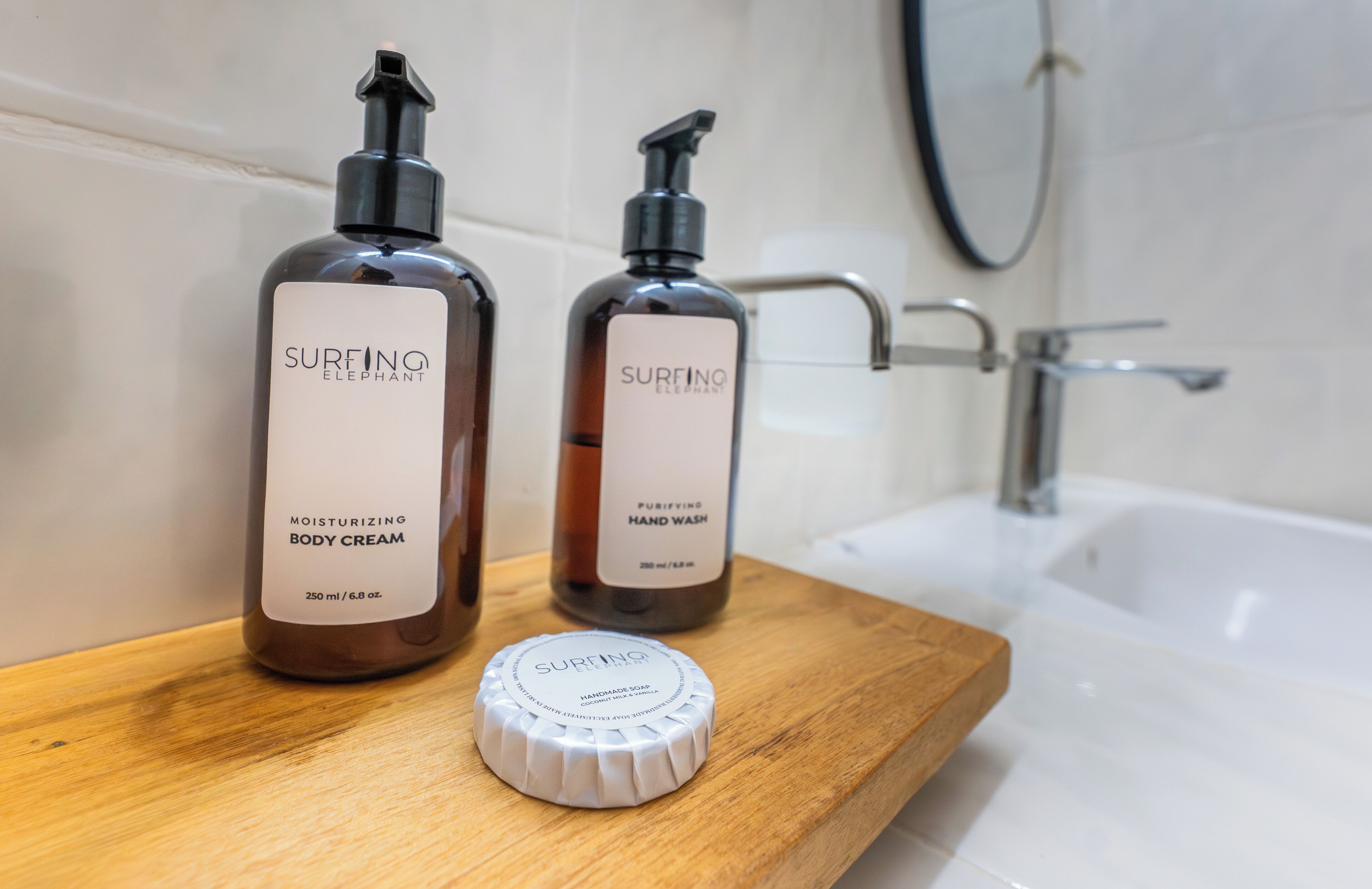 Dos botellas de crema corporal y jabón de manos Surfing Elephant sobre una superficie de madera, con una bañera al fondo.